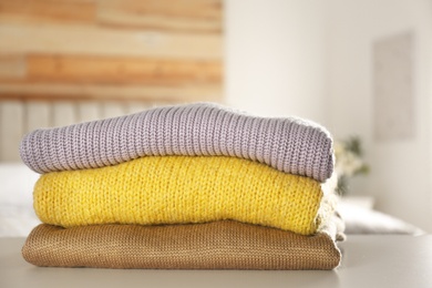 Stack of knitted sweaters on white table indoors
