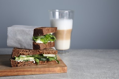 Tasty sandwiches with cream cheese, cucumber and greens on light grey table. Space for text