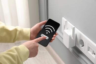 Woman with smartphone connecting to internet via wireless repeater indoors, closeup. Wi-Fi symbol on device screen