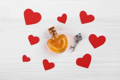 Heart shaped bottle of love potion with small key and paper hearts on white wooden table, flat lay