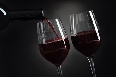 Photo of Pouring delicious red wine into glass on dark background