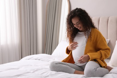 Pregnant young African-American woman sitting on bed at home