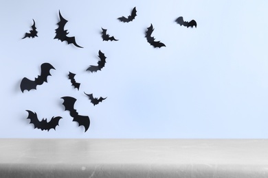 Empty grey table near white wall decorated with paper bats, space for text. Halloween celebration