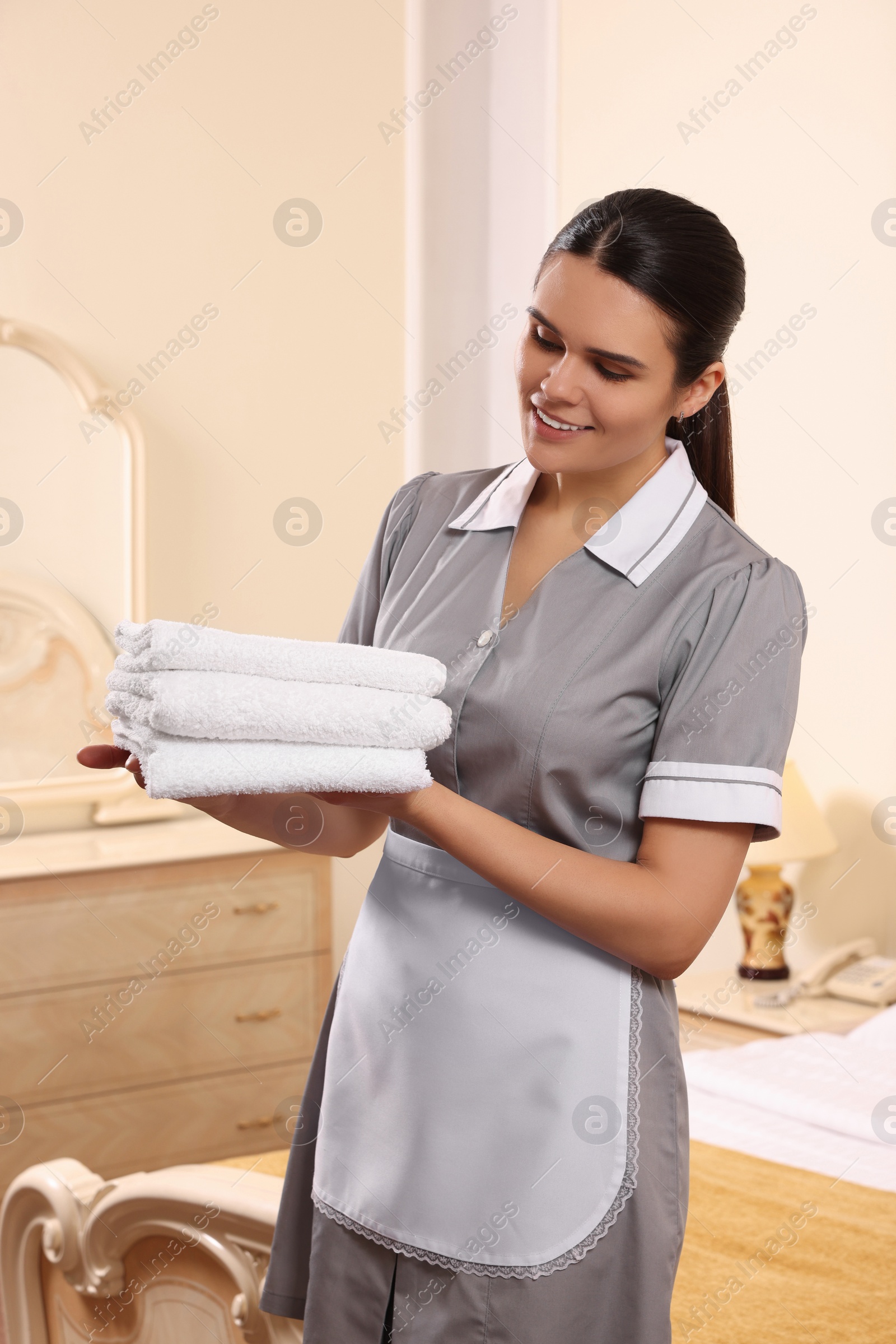 Photo of Young chambermaid holding stack of clean towels in hotel room