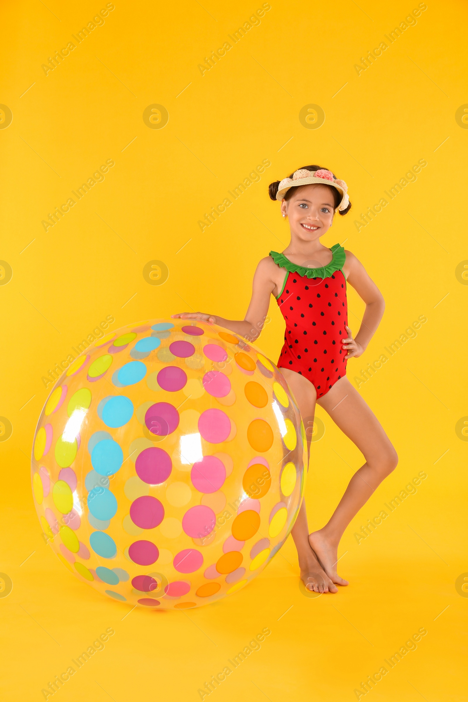 Photo of Cute little child in beachwear with bright inflatable ball on yellow background