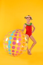 Cute little child in beachwear with bright inflatable ball on yellow background