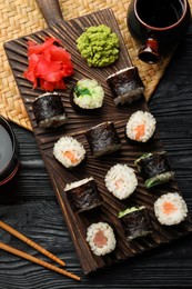 Photo of Tasty sushi rolls served on black wooden table, flat lay