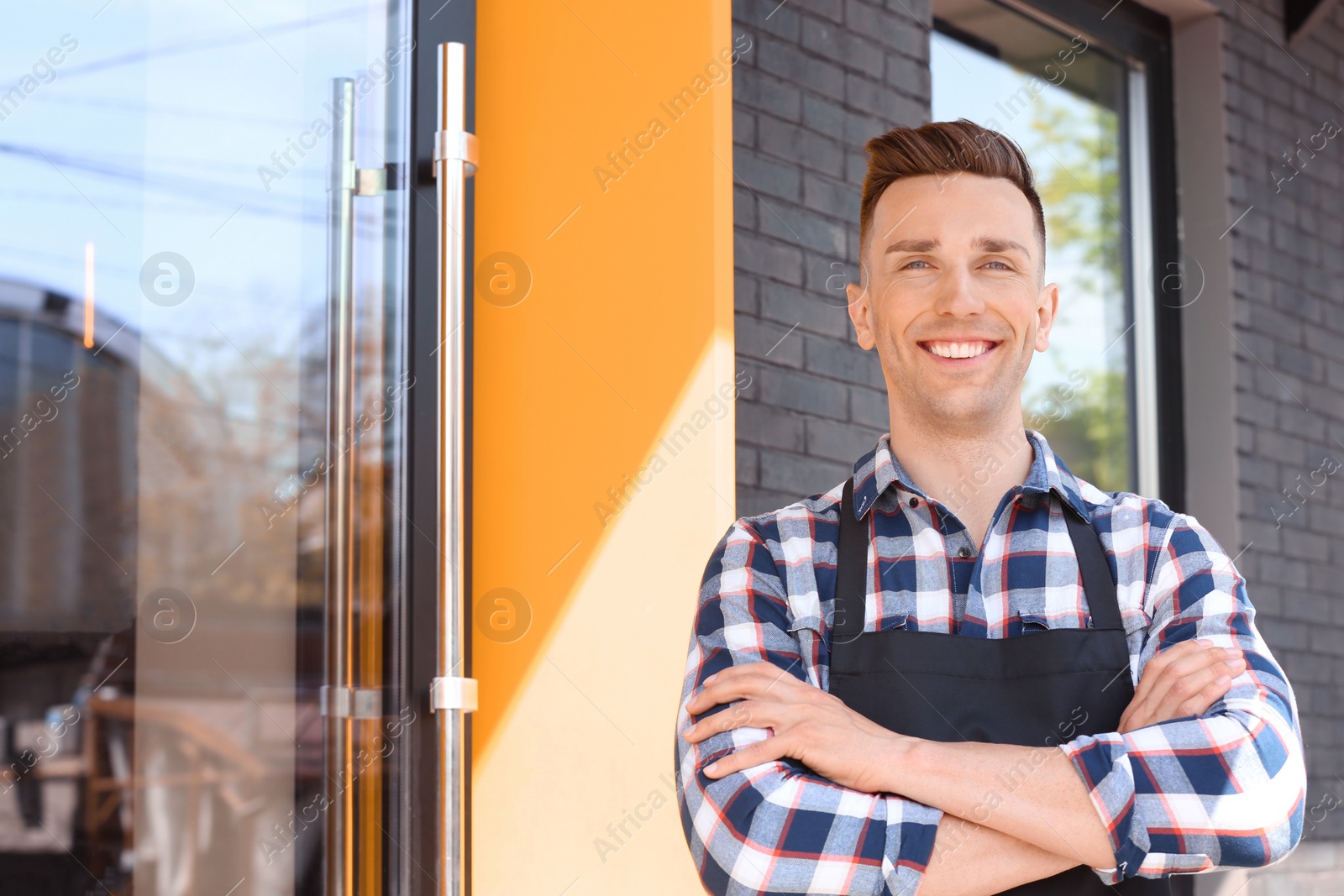 Photo of Portrait of young waiter in uniform near restaurant entrance outdoors