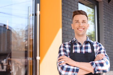 Photo of Portrait of young waiter in uniform near restaurant entrance outdoors