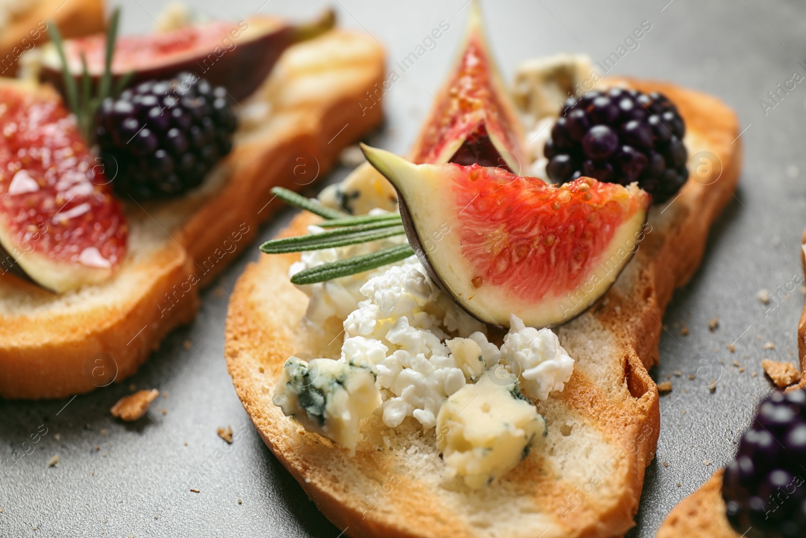 Photo of Bruschettas with cheese, figs and blackberries on grey table, closeup