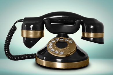 Image of Vintage black corded telephone on pale turquoise background