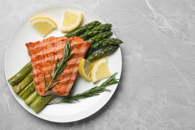 Photo of Tasty grilled salmon with asparagus, lemon and rosemary on light grey table, top view. Space for text