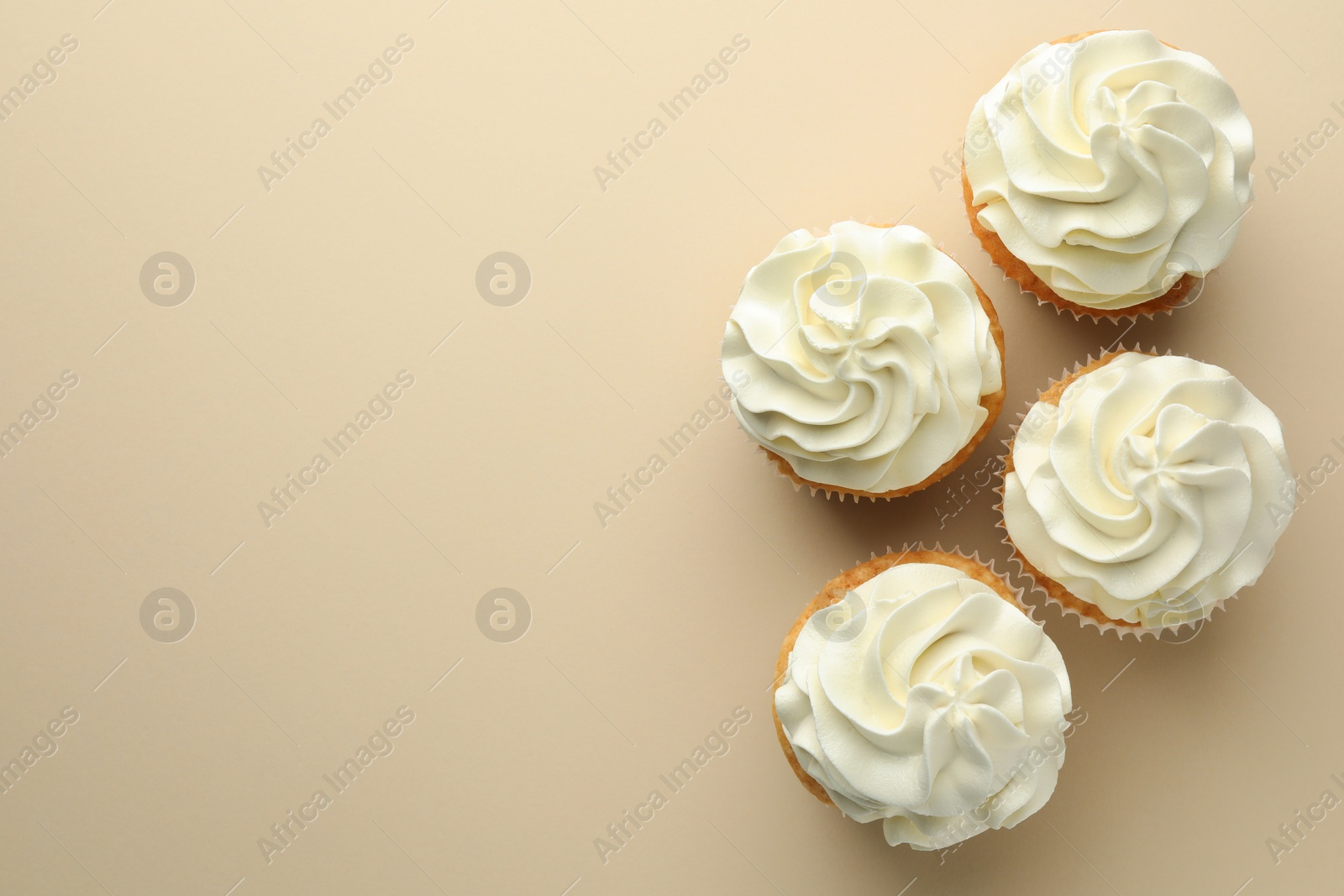 Photo of Tasty vanilla cupcakes with cream on beige background, top view. Space for text