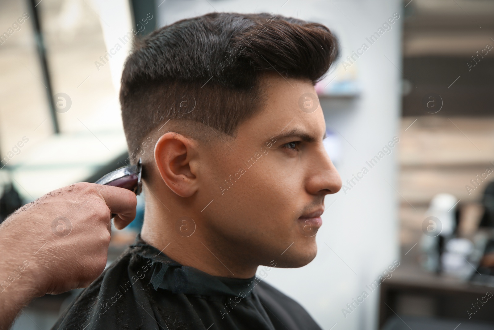 Photo of Professional barber making stylish haircut in salon, closeup