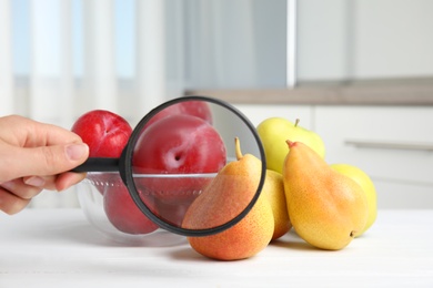 Photo of Woman with magnifying glass exploring fruits indoors, closeup. Poison detection