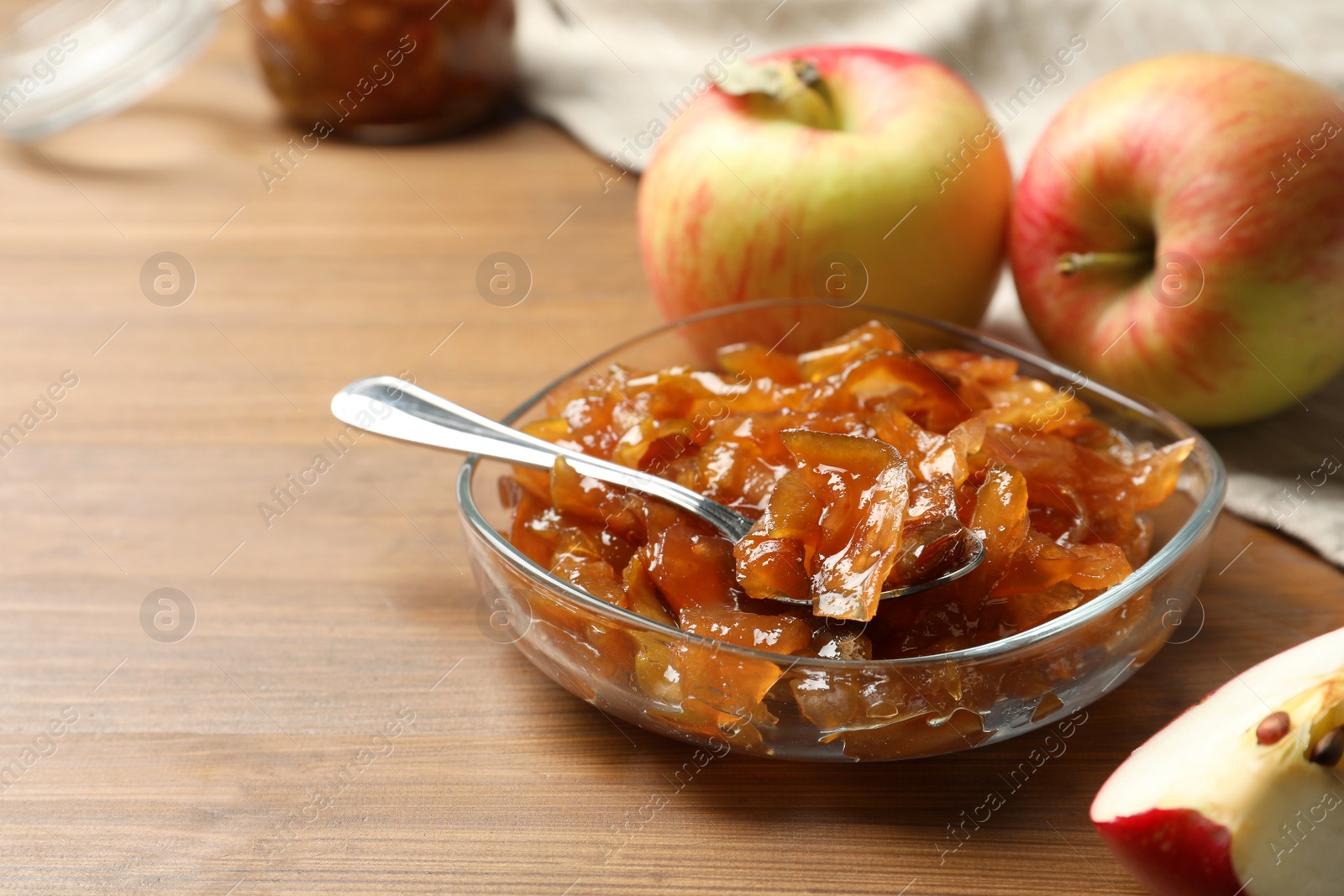 Photo of Tasty apple jam in glass bowl and fresh fruits on wooden table, space for text