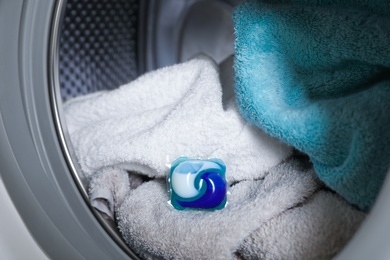 Photo of Laundry detergent capsule and towels in washing machine drum, closeup view