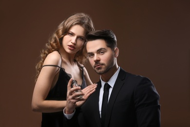 Passionate woman and handsome man using perfume on color background