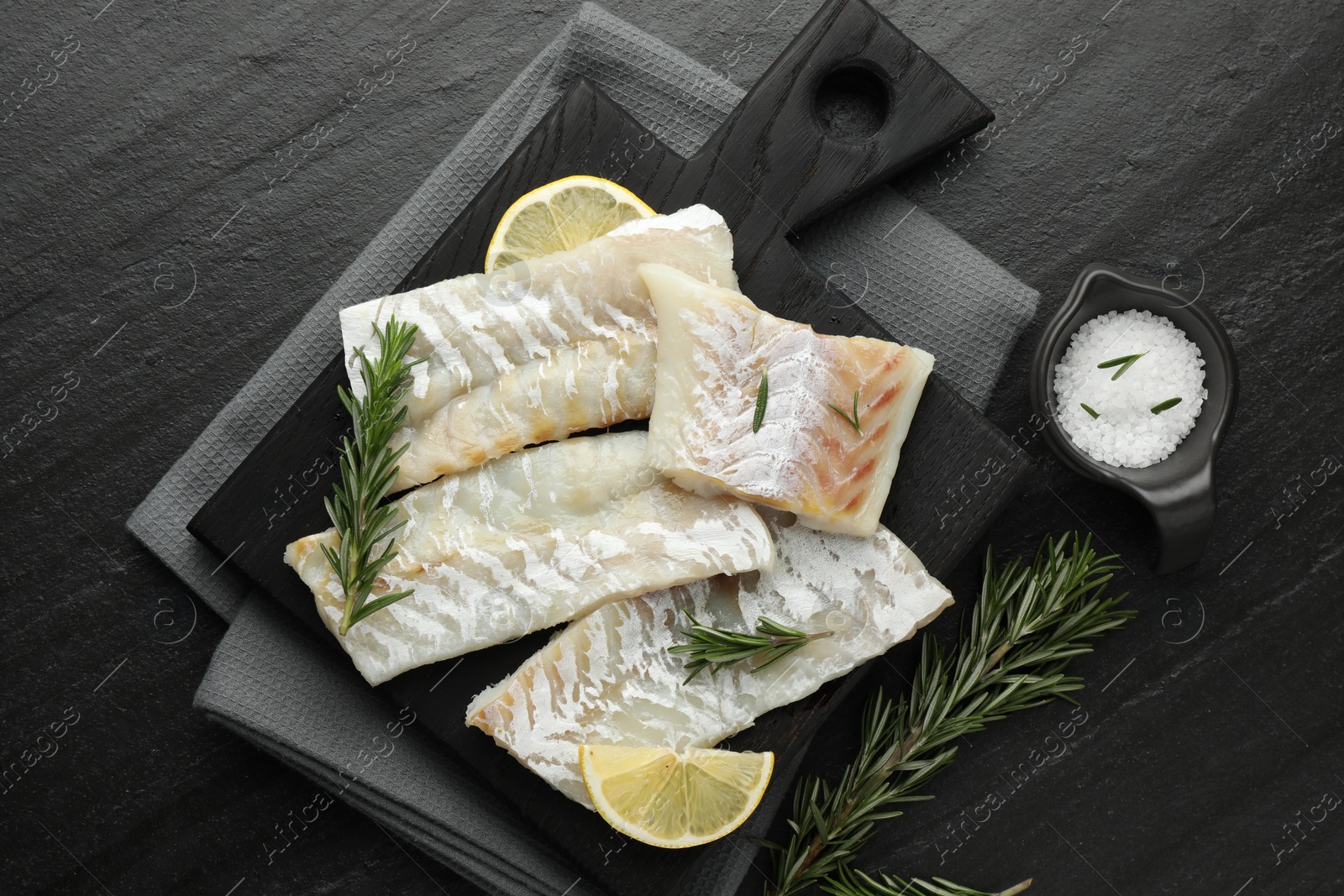 Photo of Fresh raw cod fillets, rosemary, lemon and salt on black table, flat lay