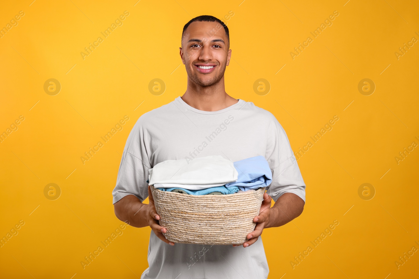 Photo of Happy man with basket full of laundry on orange background