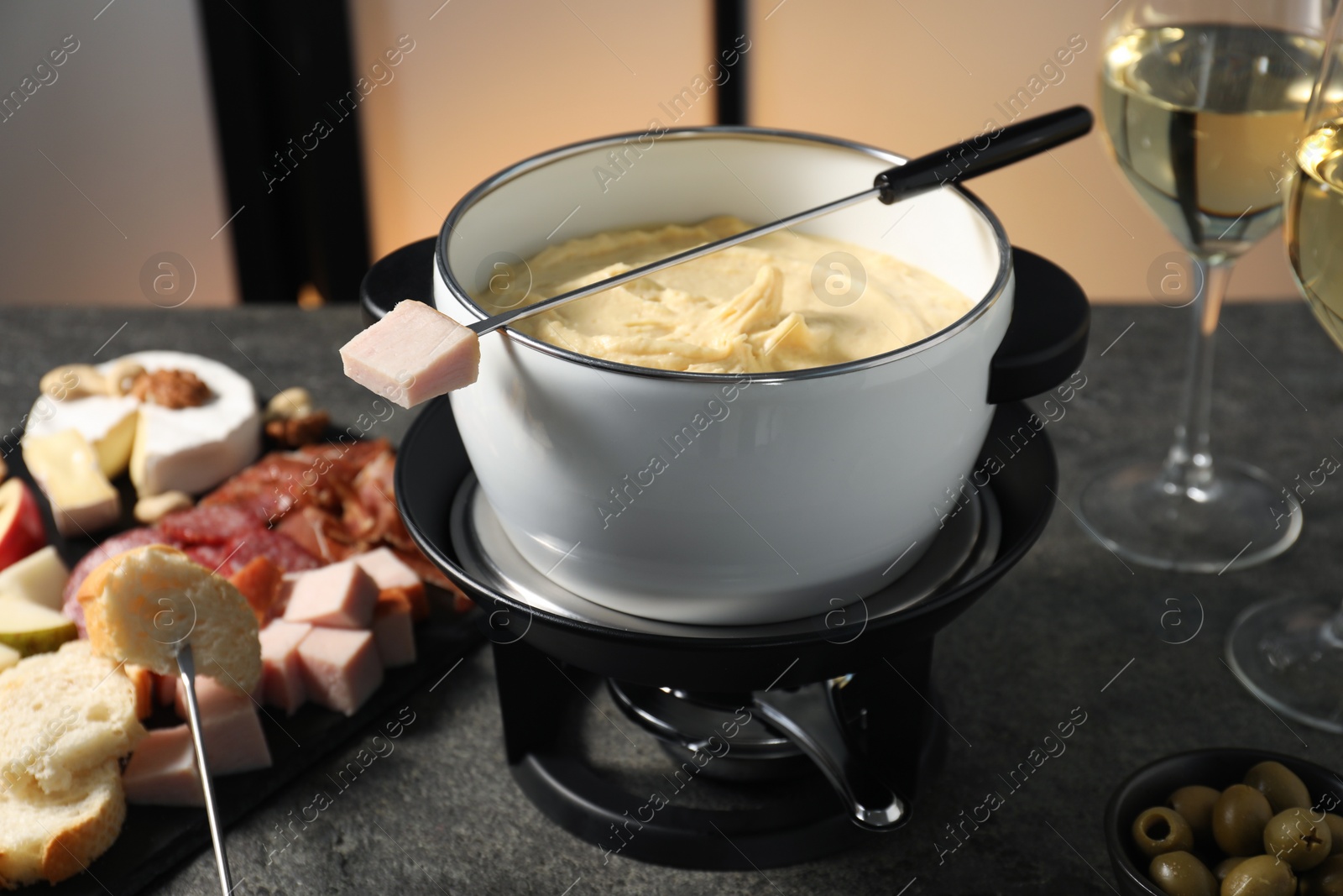 Photo of Forks with pieces of ham, bread and fondue pot with melted cheese on grey table, closeup