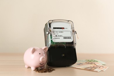 Electricity meter, piggy bank and money on wooden table