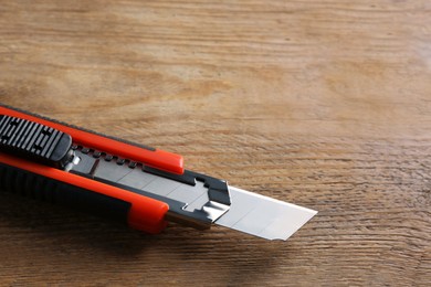 Photo of Utility knife on wooden table, closeup. Space for text