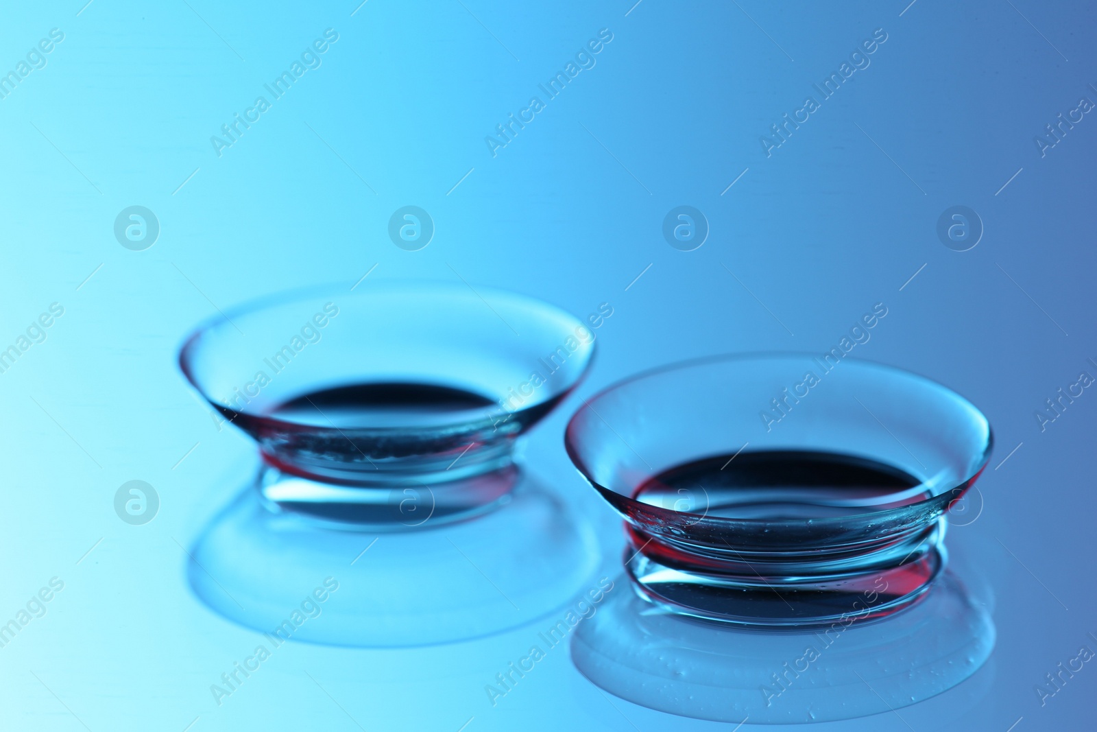 Photo of Pair of contact lenses on mirror surface, closeup. Toned in blue