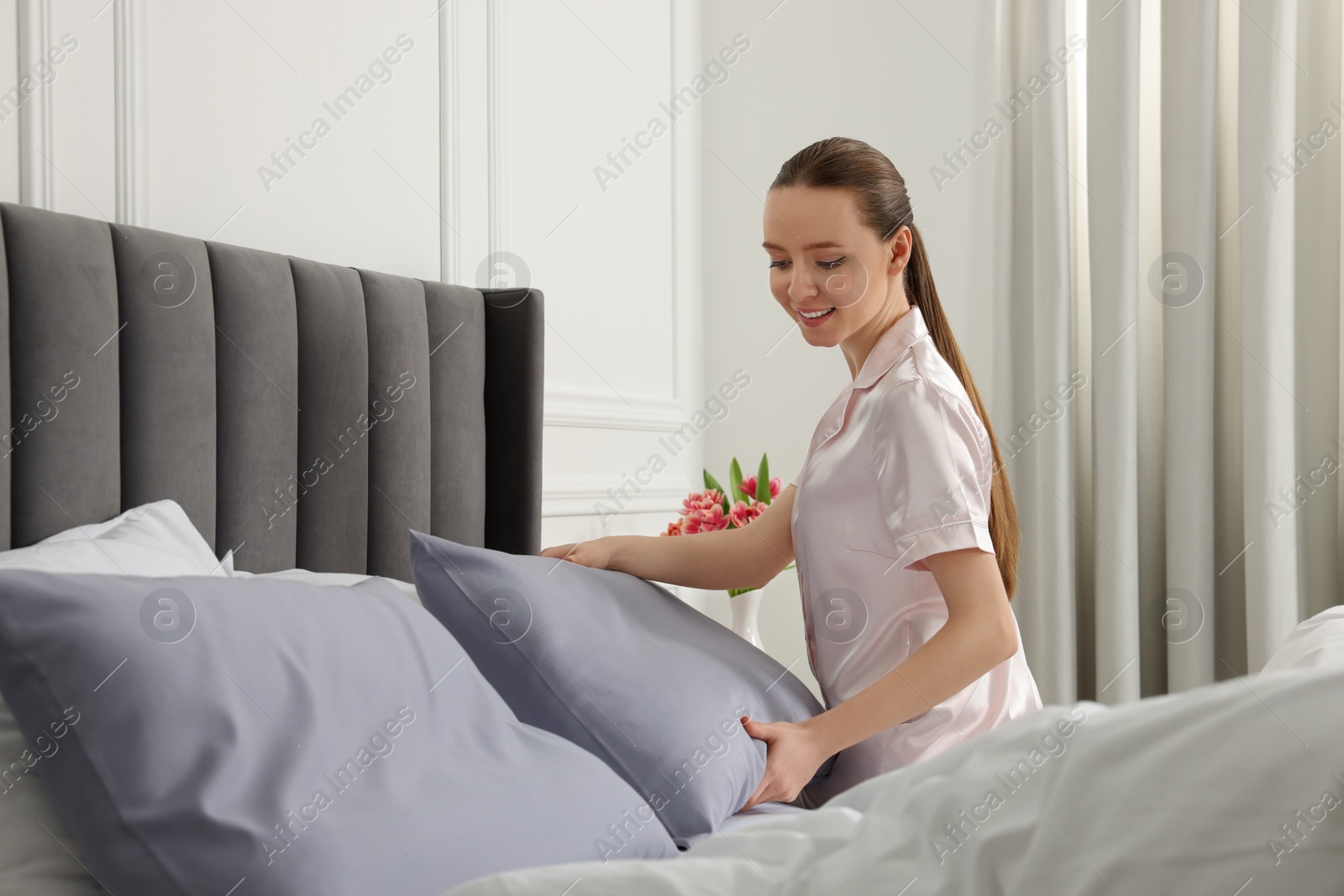 Photo of Young woman making bed in room. Space for text