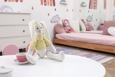 Photo of Toy bunny and cup on white table in child's bedroom. Montessori interior