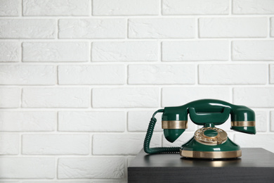 Photo of Green vintage corded phone on small black table near white brick wall. Space for text