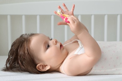 Photo of Cute little baby with toothbrush in comfortable crib at home