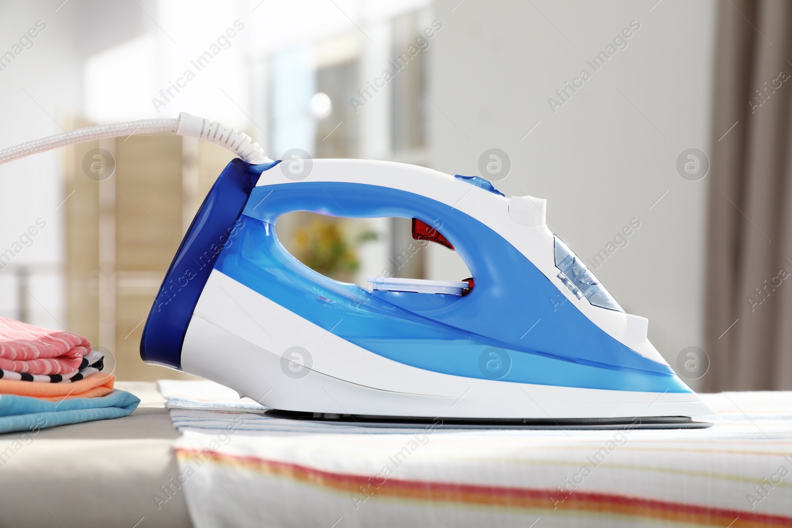 Photo of Modern electric iron on board indoors. Household appliance