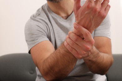 Photo of Man suffering from pain in his hand on sofa indoors, closeup