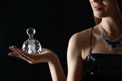 Young woman with bottle of perfume on black background, closeup