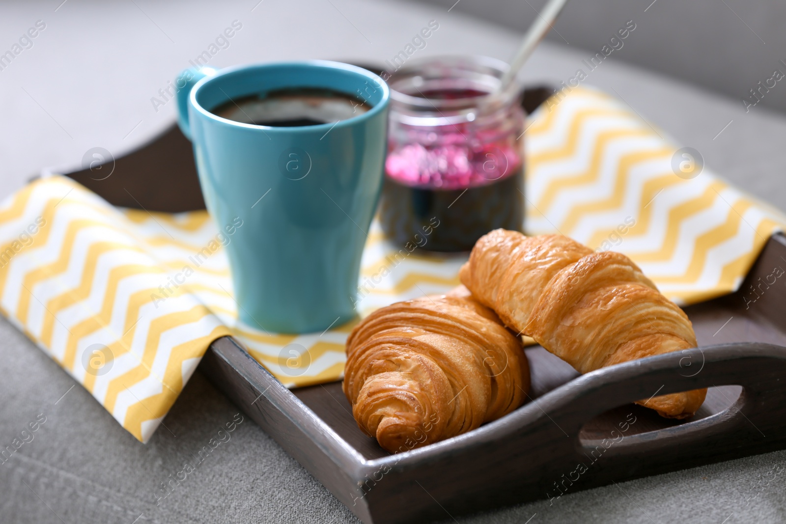 Photo of Fresh croissants, cup of coffee and jar with jam on tray