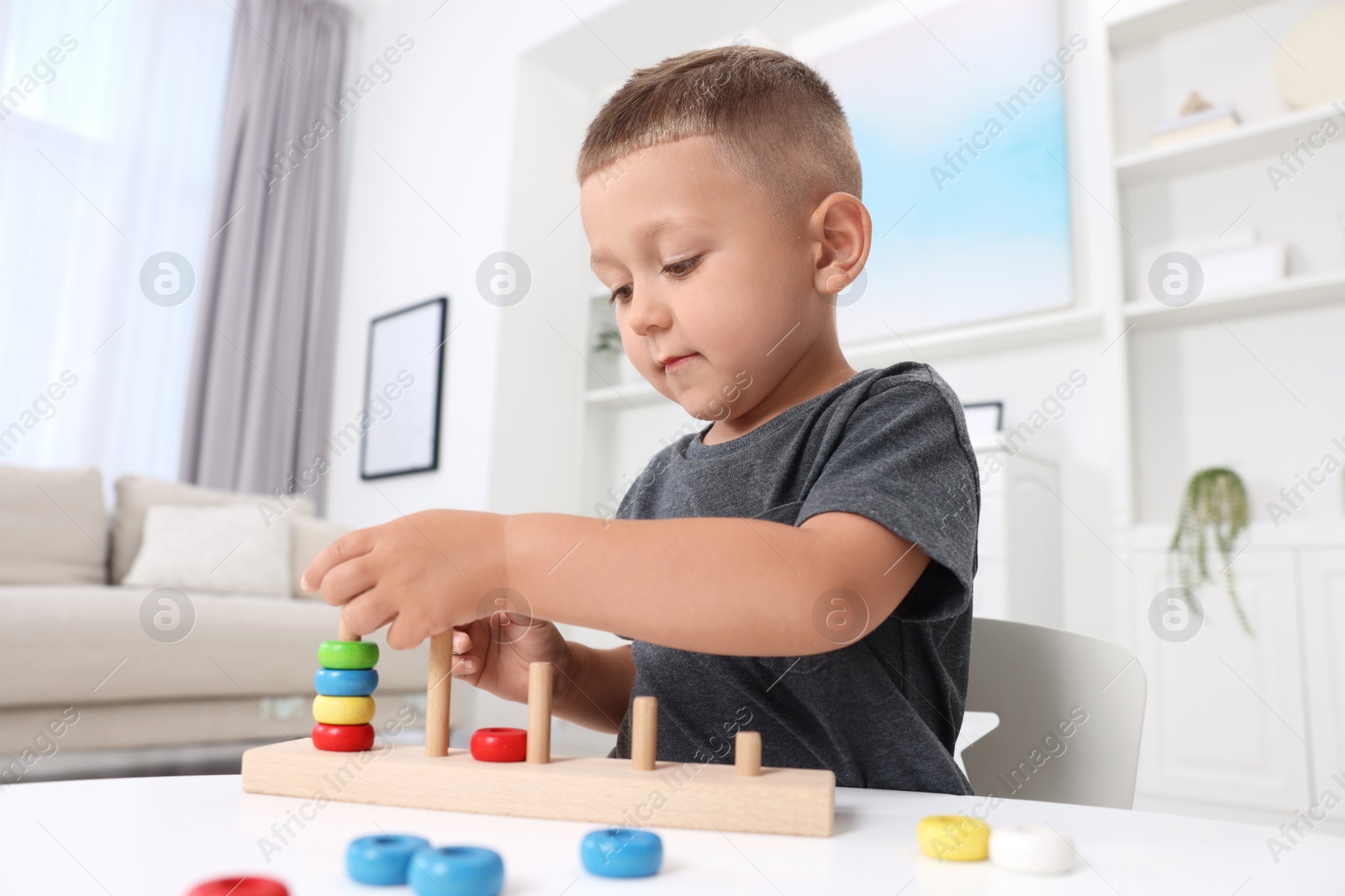 Photo of Motor skills development. Little boy playing with stacking and counting game at table indoors