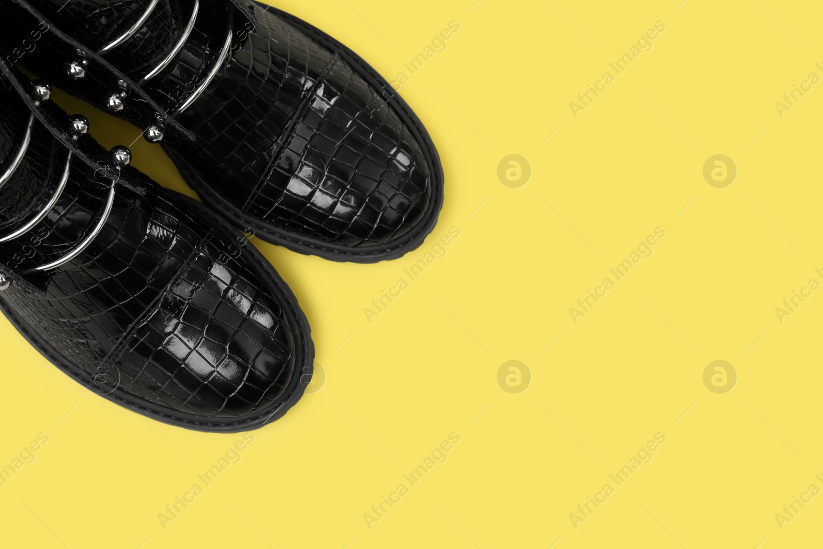 Photo of Pair of stylish ankle boots on yellow background, top view. Space for text