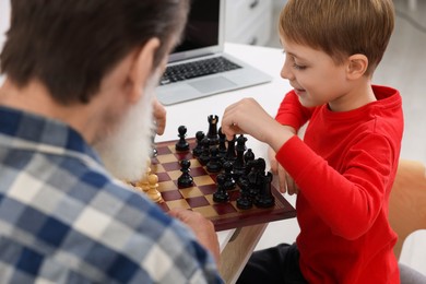 Grandfather and grandson playing chess at table indoors, closeup