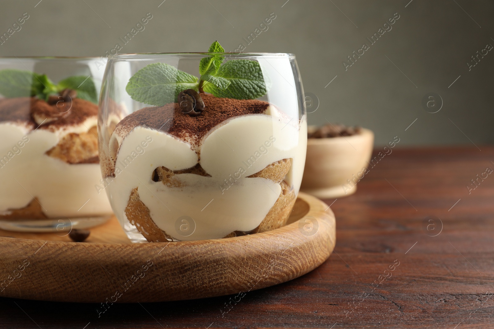 Photo of Delicious tiramisu in glasses, mint leaves and coffee beans on wooden table, closeup. Space for text