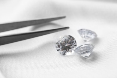 Beautiful shiny diamonds and tweezers on white fabric, closeup