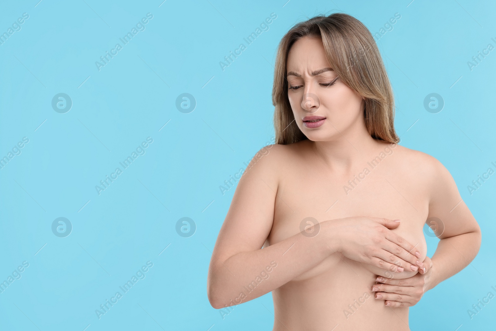 Photo of Mammology. Naked young woman doing breast self-examination on light blue background, space for text