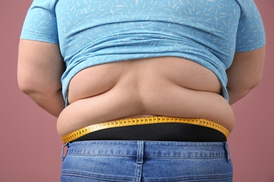 Photo of Overweight woman with measuring tape on color background