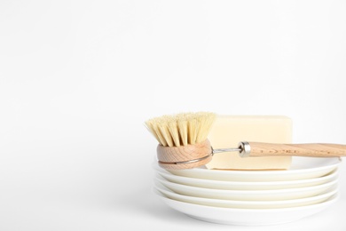 Cleaning brush and soap bar for dish washing on plates against white background