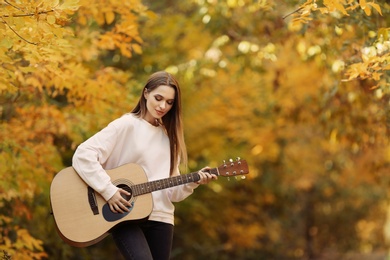 Teen girl playing guitar in autumn park