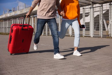Photo of Being late. Couple with red suitcase running outdoors, closeup
