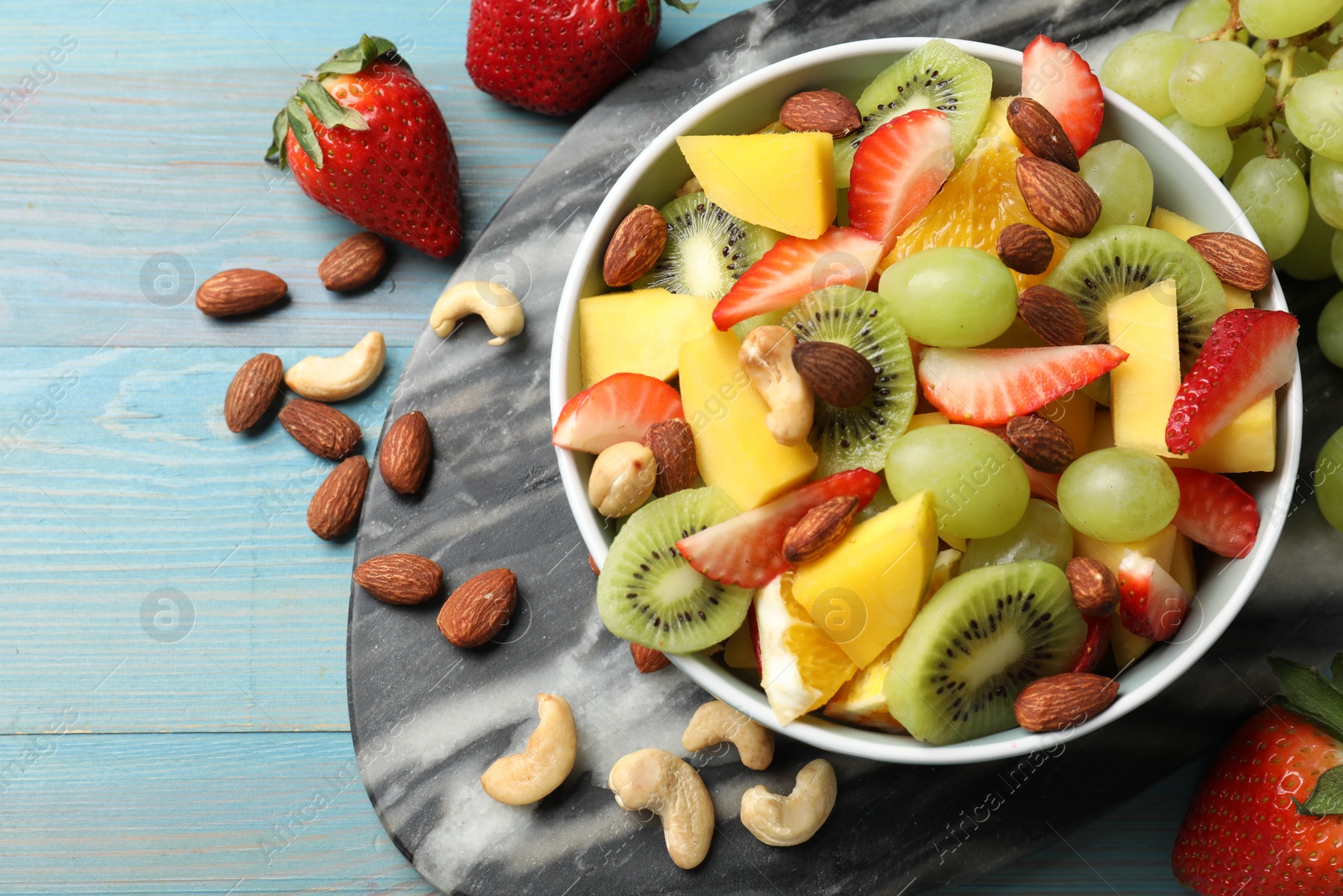 Photo of Tasty fruit salad in bowl and ingredients on light blue wooden table, flat lay