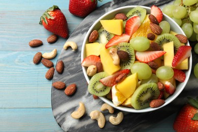 Tasty fruit salad in bowl and ingredients on light blue wooden table, flat lay