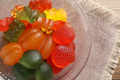 Different delicious gummy candies in glass bowl on table, top view