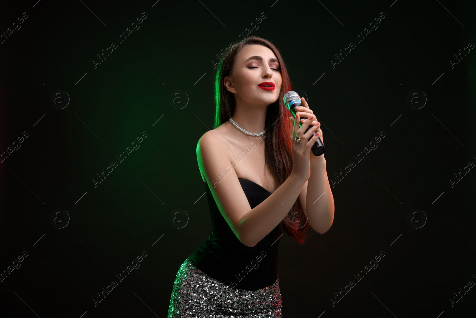 Photo of Emotional woman with microphone singing in color lights on dark background